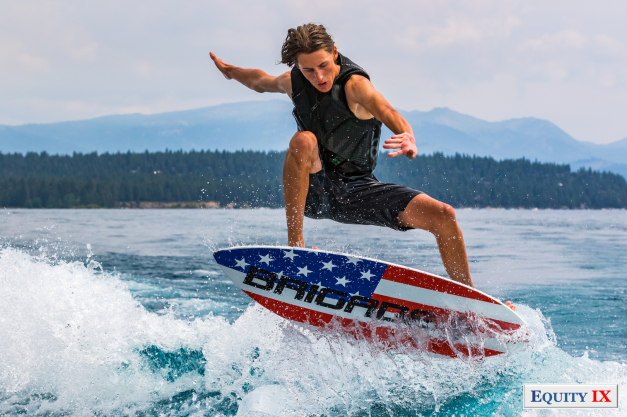 Cole Sorenson jumps a wake on a Brigade red, white and blue wake-surf board with mountains in the background of Lake Tahoe © Equity IX - SportsOgram - Leigh Ernst Friestedt